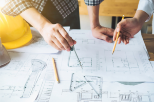 Hands holding pencils hover over building schematics