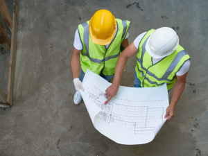 A birds eye view of two men in hardhats looking over building schematics