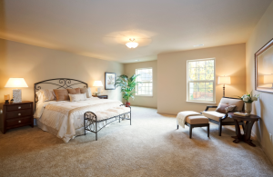 A bedroom with neutral tones. The room has a bed, bedside table, table and chairs.