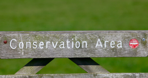 A weathered wooden sign reads "Conservation Area" in white letters, set against a backdrop of lush green grass, conveying a peaceful, natural setting.